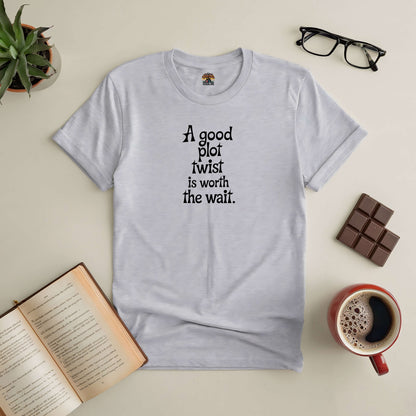 "A Good Plot Twist is Worth The Wait tee for readers, surrounded by an open book, coffee, glasses, and chocolate bar on a table"