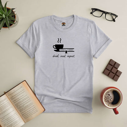 "Drink. Read. Repeat. tee with coffee cup and book design, surrounded by a book, glasses, plant, chocolate, and coffee mug."