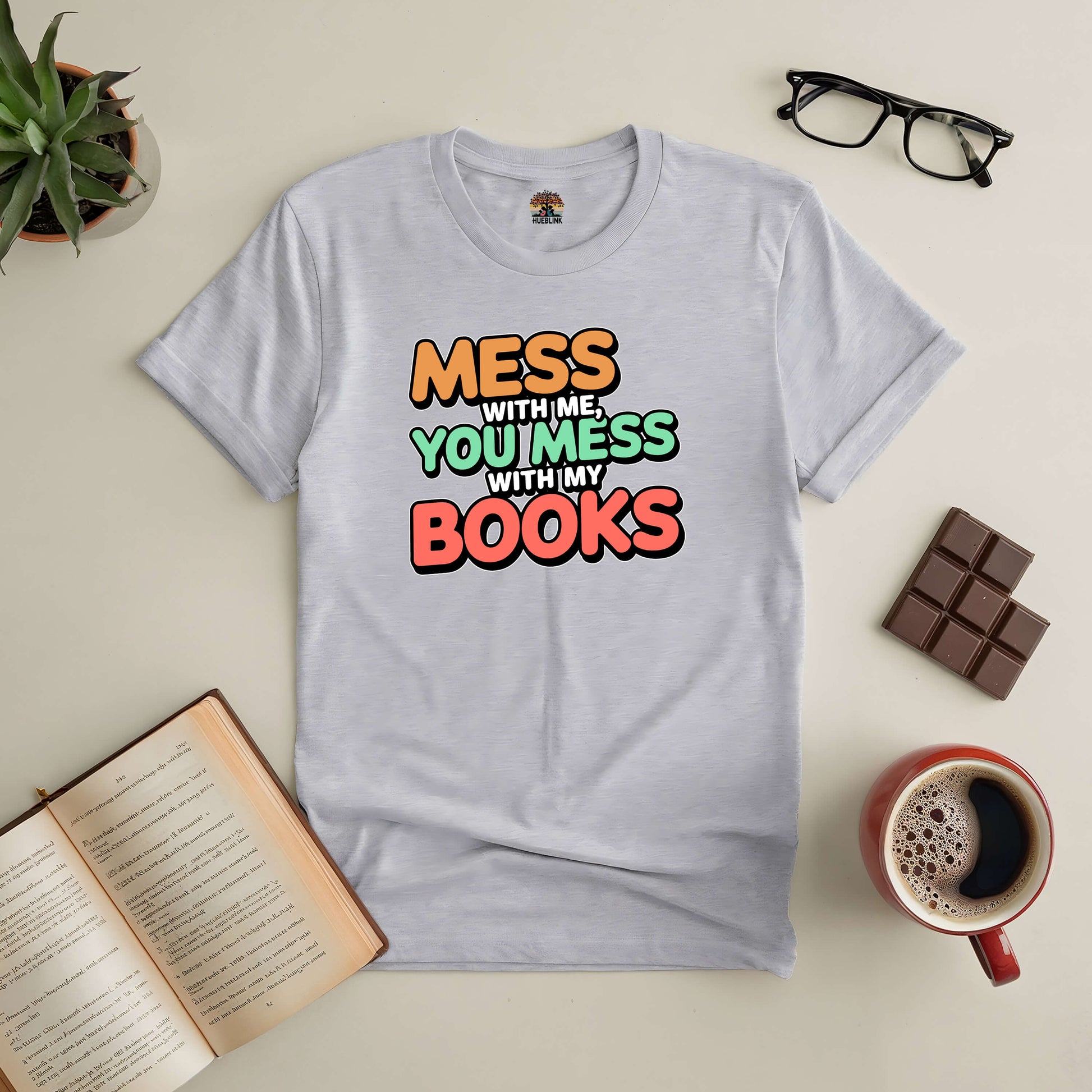 "Mess With Me You Mess With My Books Tee for book lovers, surrounded by glasses, coffee, chocolate, and an open book on a table"