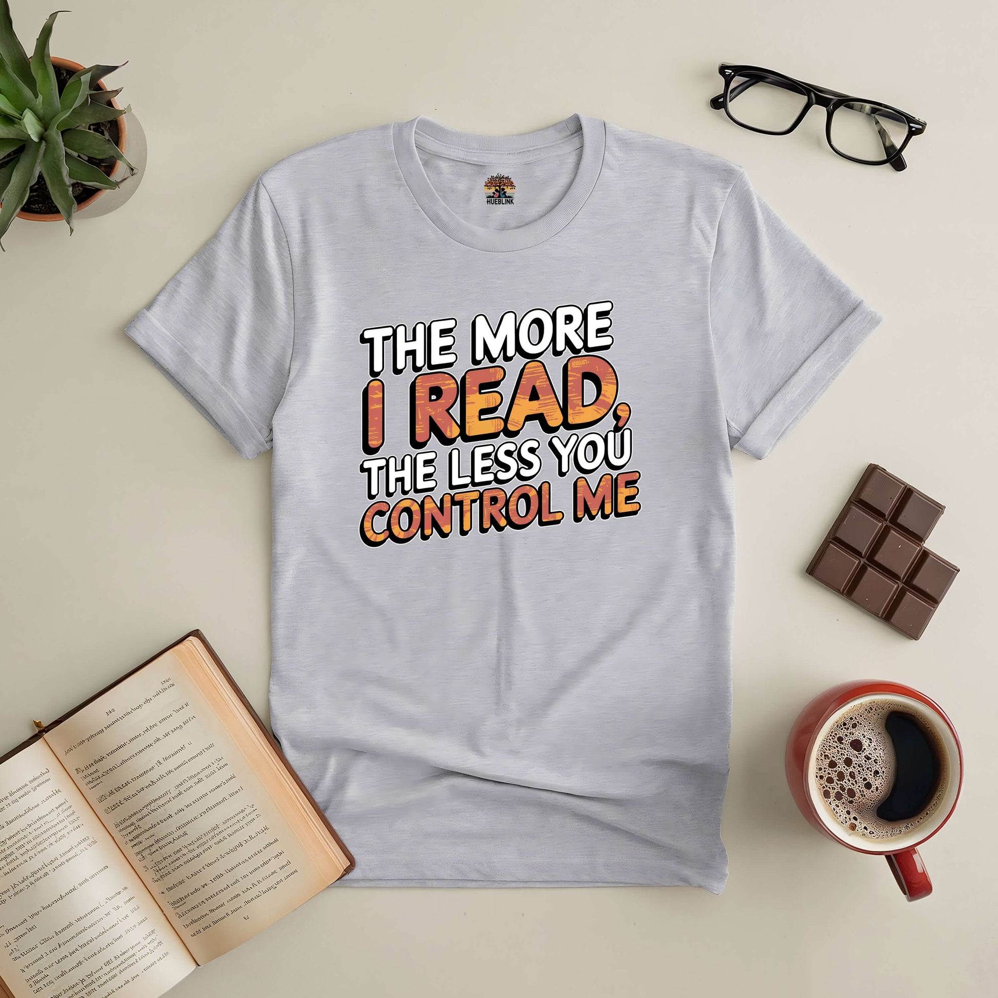 Gray T-shirt with "The More I Read, The Less You Control Me" text, surrounded by books, glasses, coffee, and chocolate.