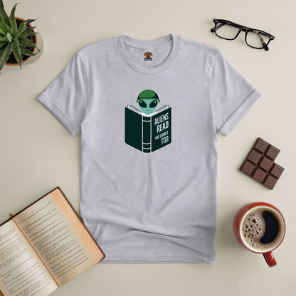 "Intergalactic Habit Tee with alien reading design for book lovers and sci-fi fans, surrounded by open book, coffee, and chocolate"