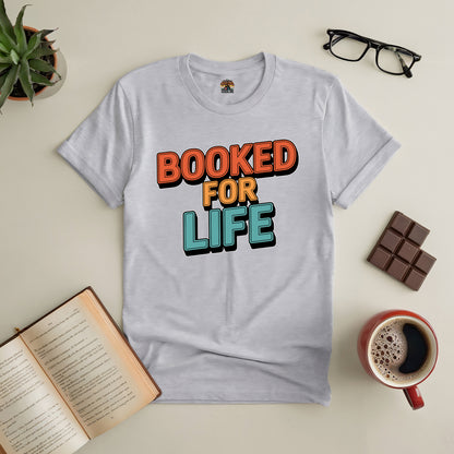 "White 'Booked for Life' tee for avid readers, styled with open book, glasses, coffee, and chocolate on a table"