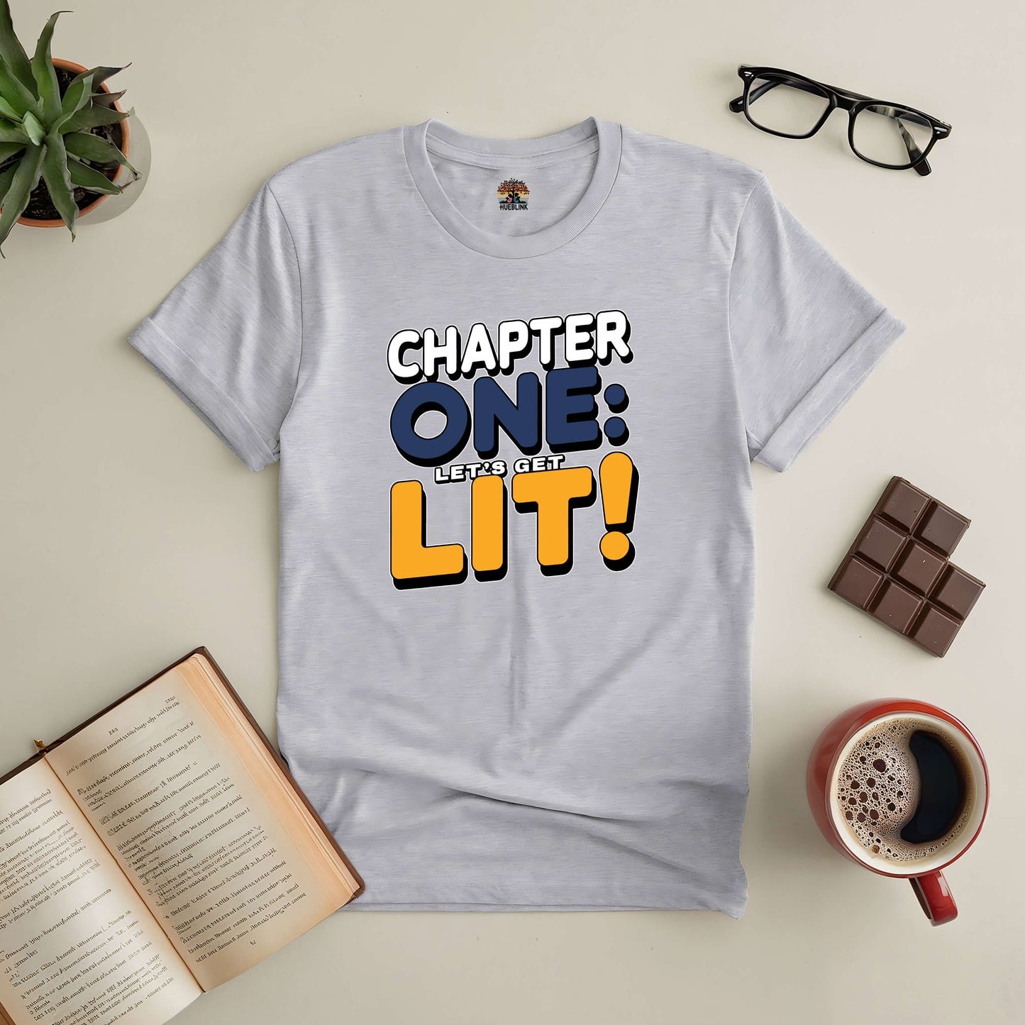 Chapter One: Let’s Get Lit! Tee for book lovers and party enthusiasts, with open book, coffee, and chocolate arrangement.