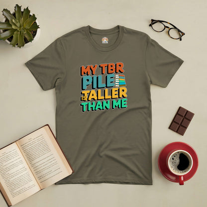 "My TBR Pile is Taller Than Me tee with colorful text, surrounded by books, coffee, chocolate, glasses, and a plant."