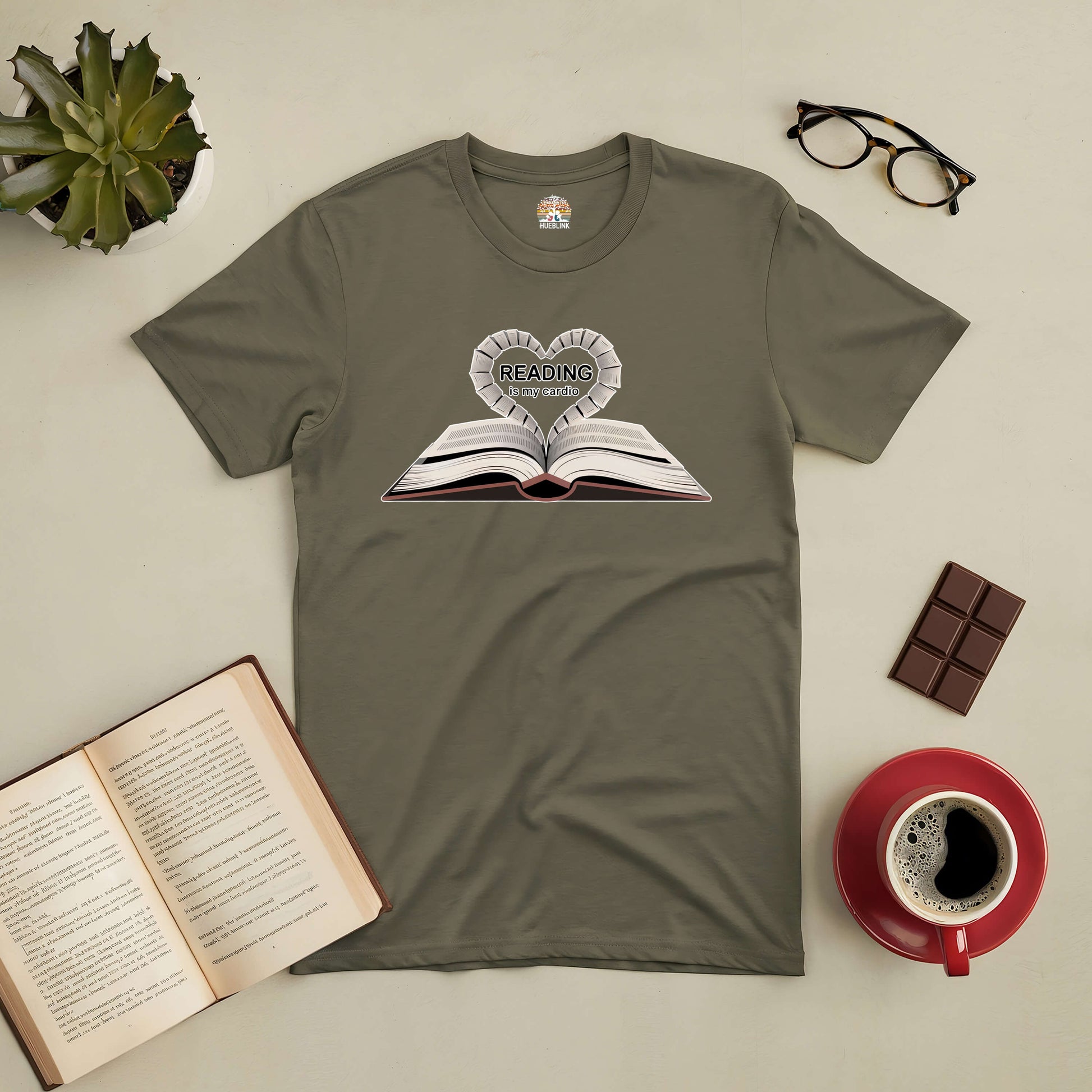 "Reading Is My Cardio Tee featuring open book design, perfect for book lovers, displayed with coffee, glasses, and chocolate"