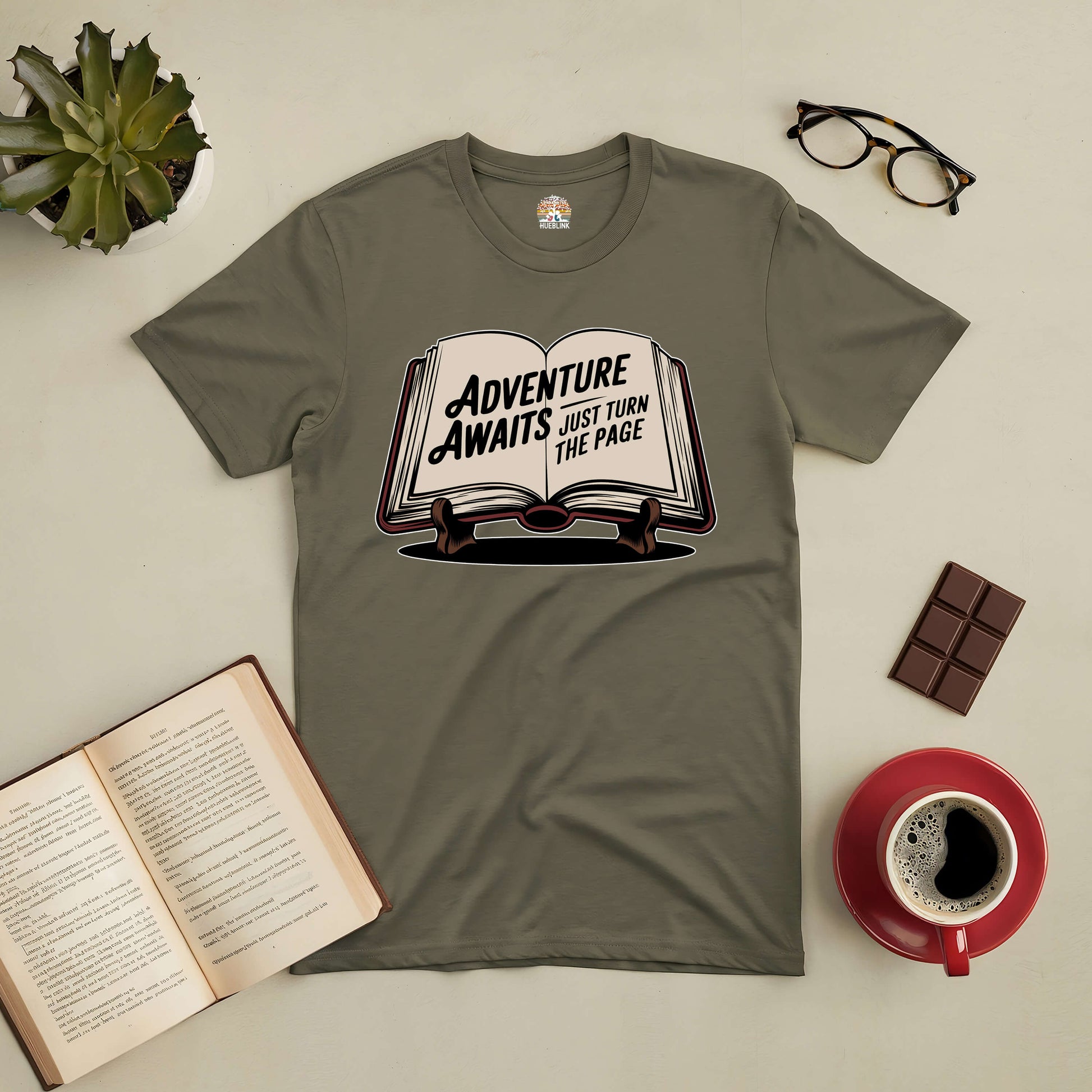 Olive green t-shirt with 'Adventure Awaits: Just Turn the Page' book graphic, perfect for book lovers and adventure seekers.