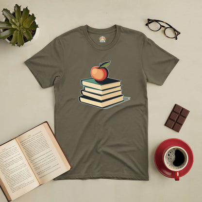 Olive green tee with stacked books and apple design for book lovers, next to open book, glasses, coffee, and chocolate.