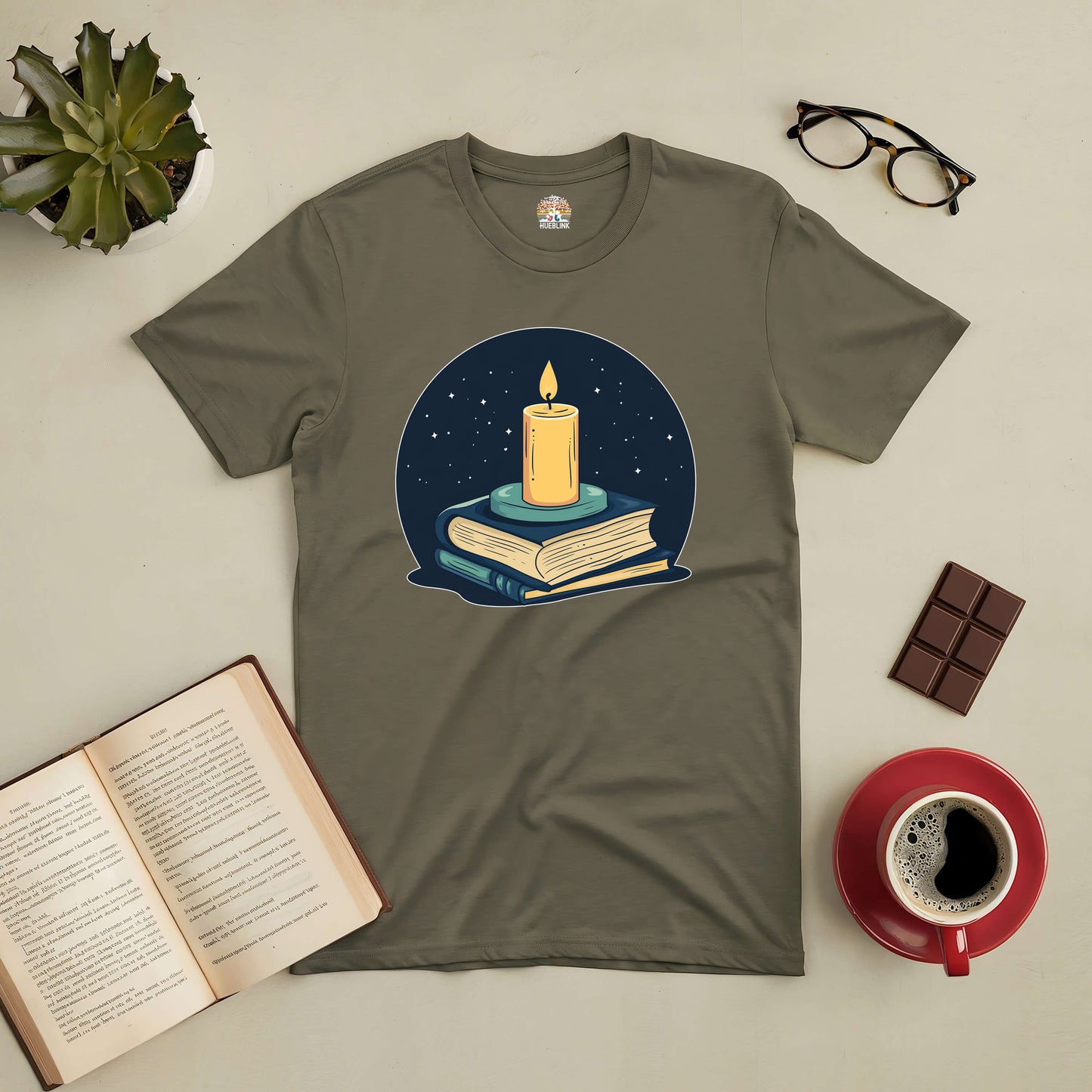 "Illuminate Your Mind Tee featuring a candle on books design, surrounded by coffee, chocolate, and glasses, ideal for book lovers."