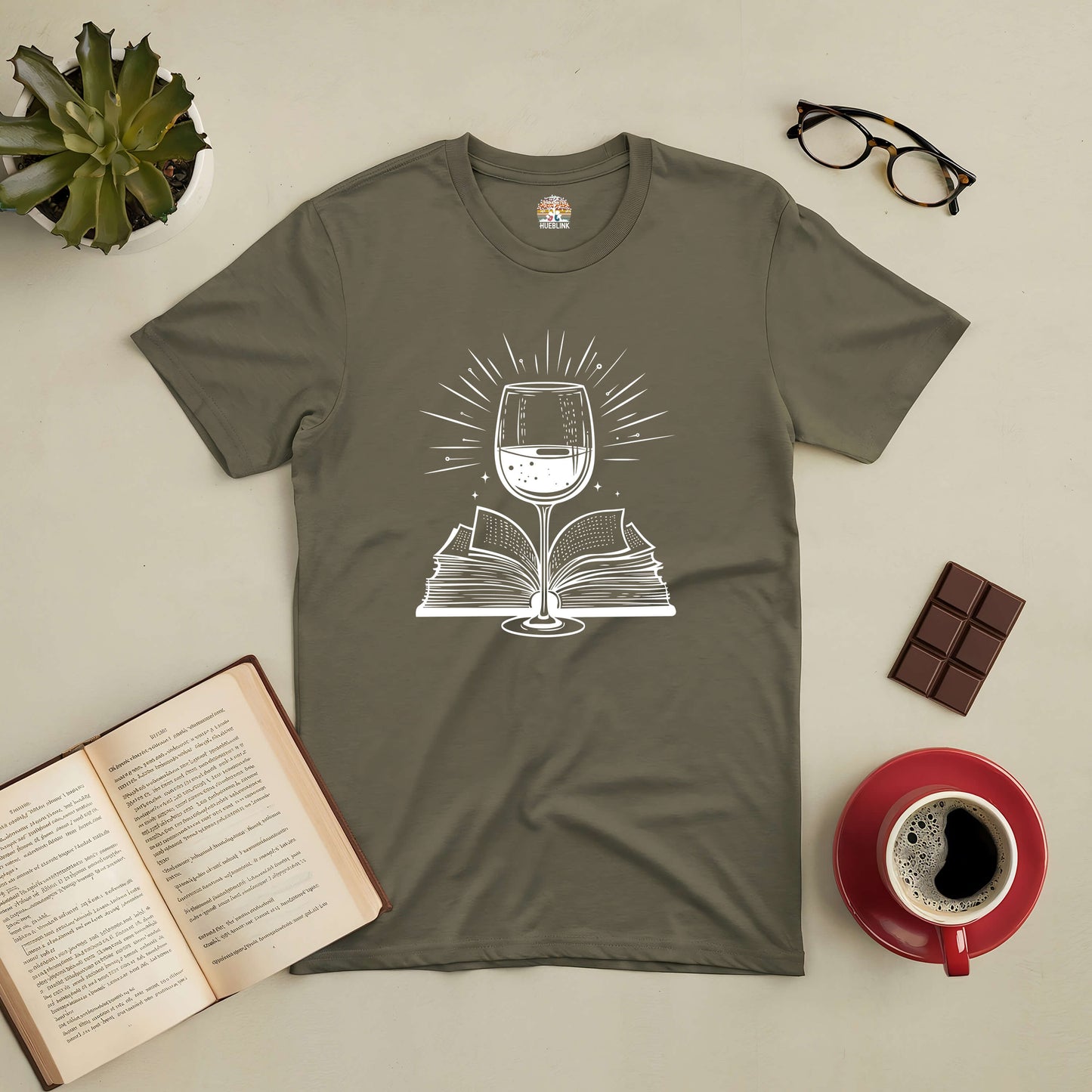 Literary Libations tee with wine glass and open book design, surrounded by glasses, coffee, chocolate, and an open book. Perfect for book lovers.