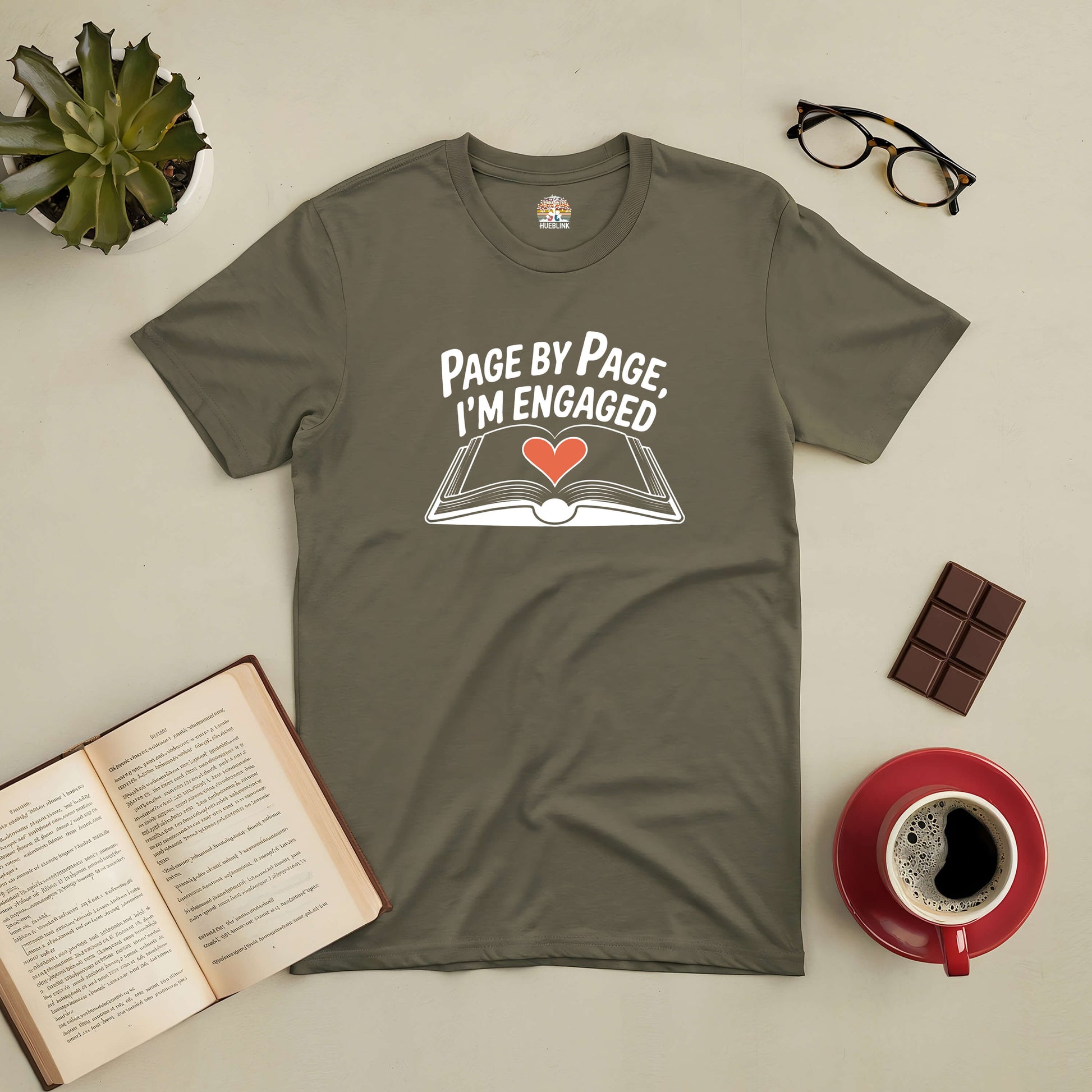 Gray "Page by Page, I’m Engaged" tee with open book and heart design, ideal for dedicated readers, shown with coffee and reading accessories.