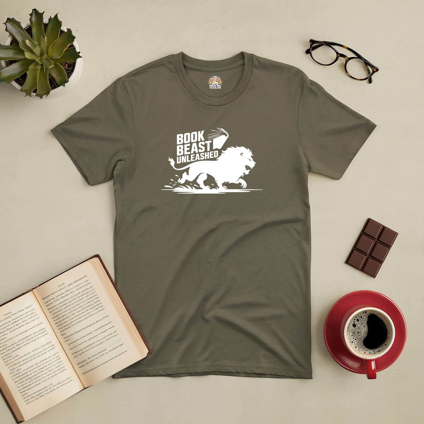 "Book Beast Unleashed Tee with lion graphic, ideal for avid readers, displayed with open book, coffee, chocolate, and glasses"