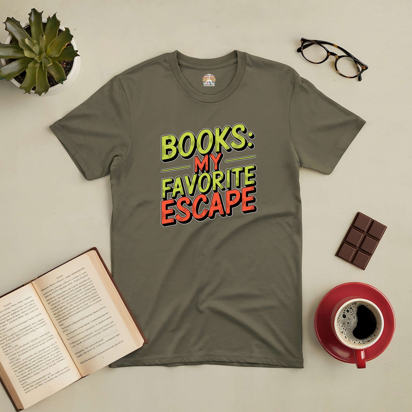 Olive green "Books: My Favorite Escape" tee with an open book, coffee cup, glasses, and chocolate bar on a table.