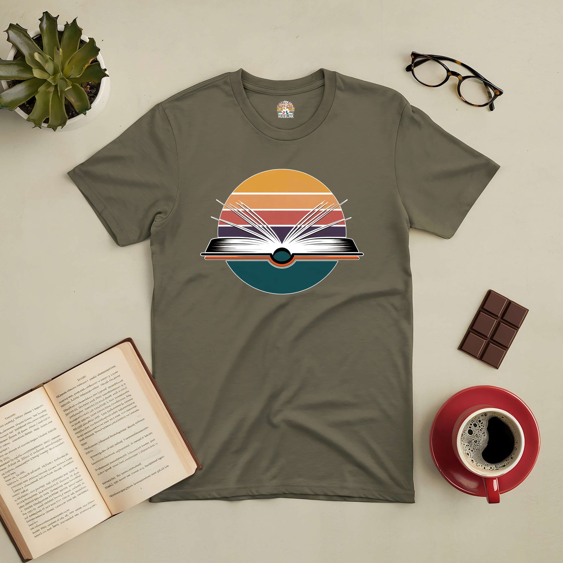 "Gateway to New Horizons Tee with open book design, surrounded by coffee, chocolate, and eyeglasses, encouraging exploration through reading."