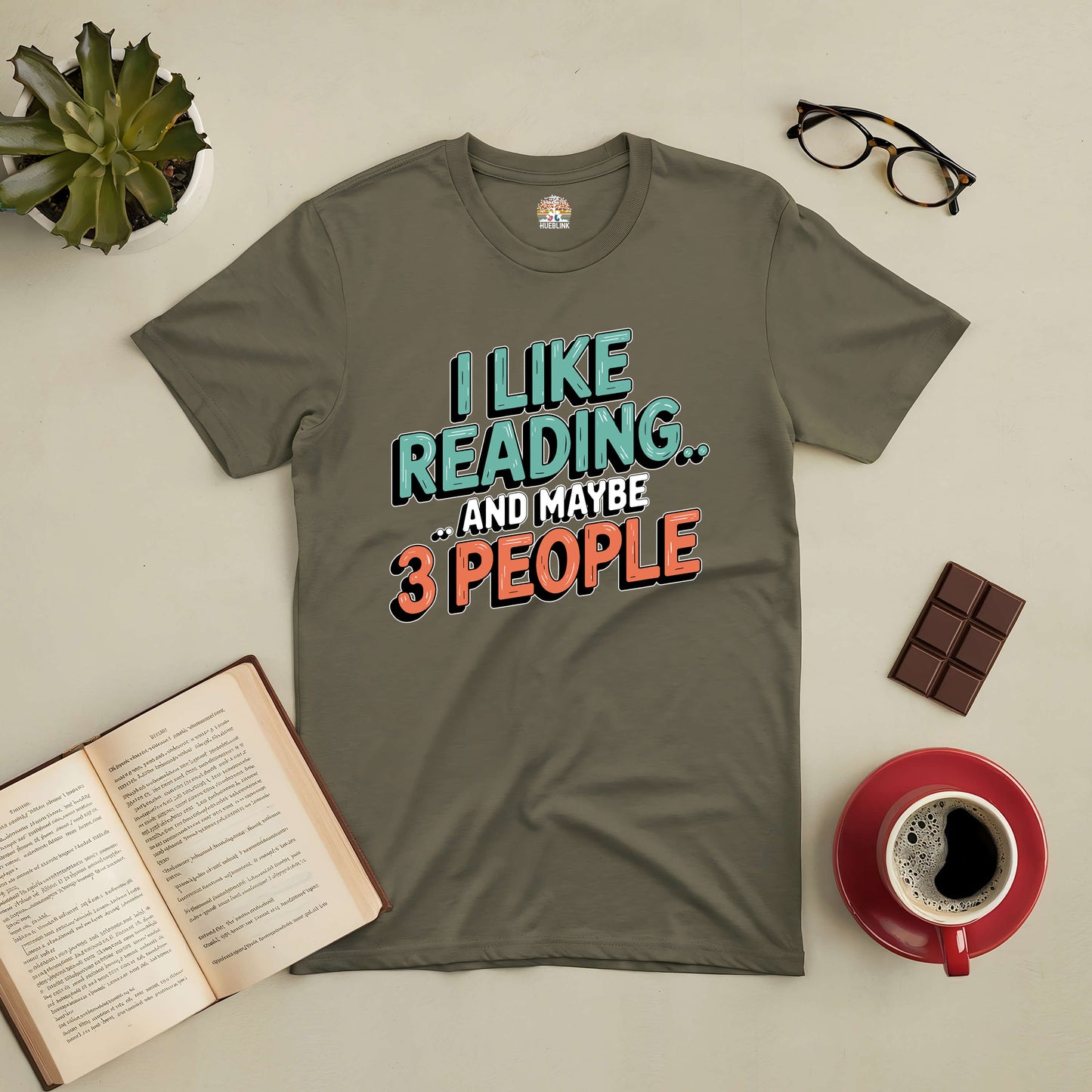 Olive green tee with the phrase "I Like Reading... and Maybe 3 People" for introverted book lovers, alongside a book, glasses, and coffee.