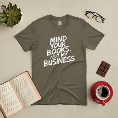 Olive green tee with "Mind Your Books, Not My Business" text next to coffee, glasses, and an open book, perfect for book lovers.