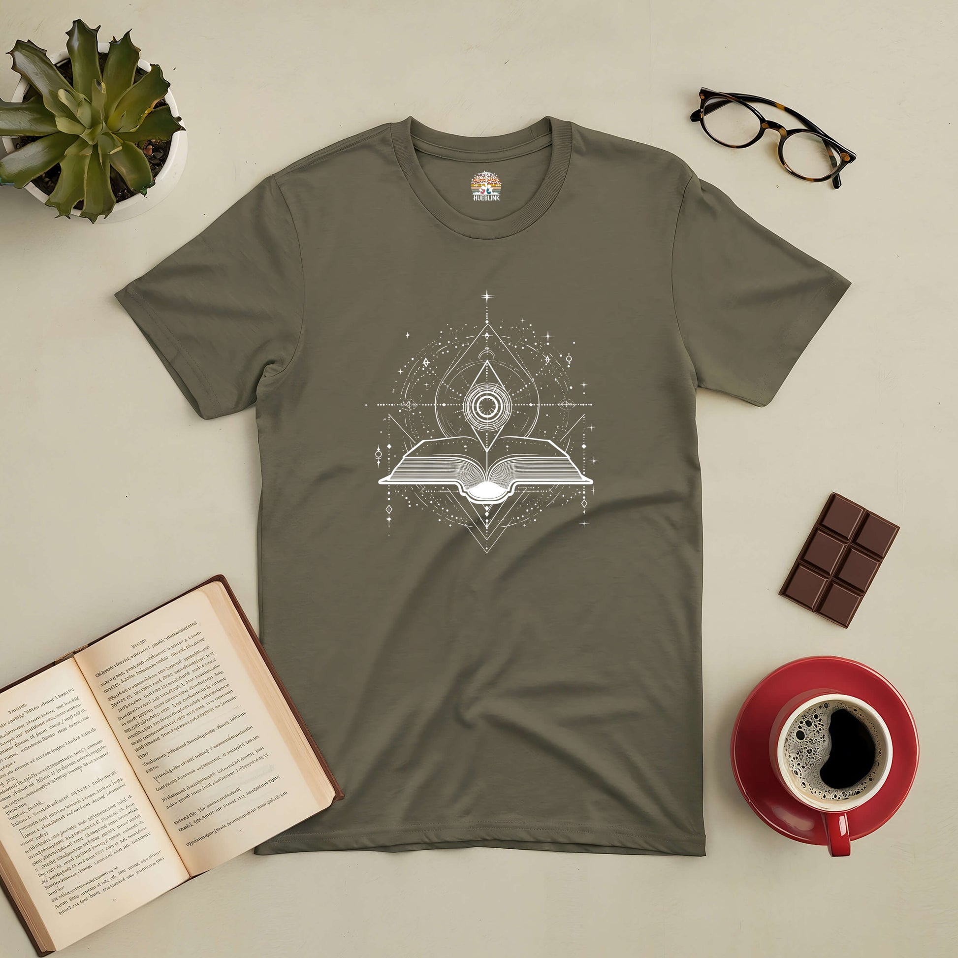 Portal to Knowledge Tee with mystical book design surrounded by coffee, open book, chocolate, glasses, and a plant.