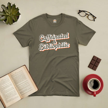 Caffeinated & Bibliophilic Tee with open book, coffee, and chocolate on a table, perfect for book and coffee lovers.