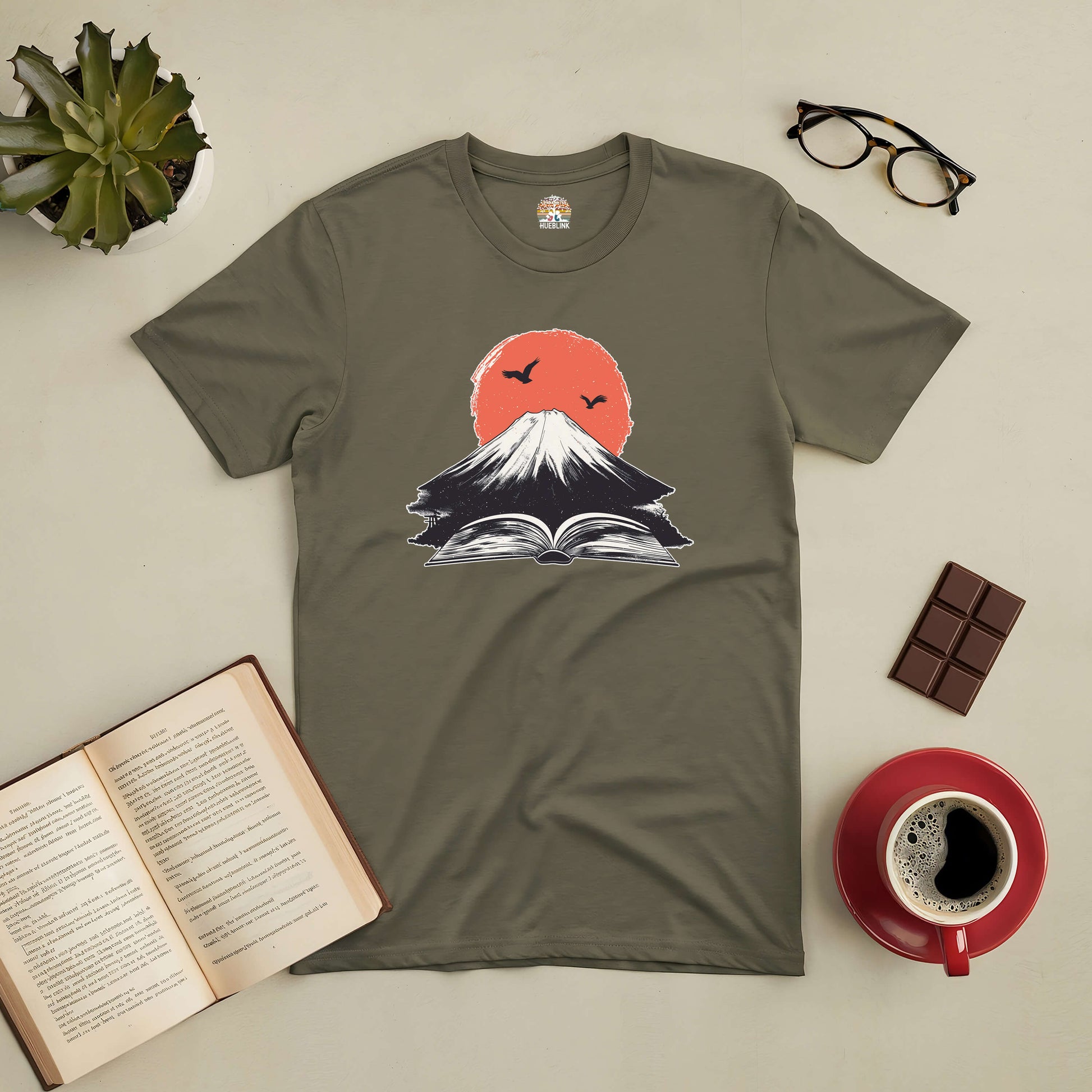 Olive t-shirt featuring erupting volcano and open book design, symbolizing adventurous imagination sparked by reading.