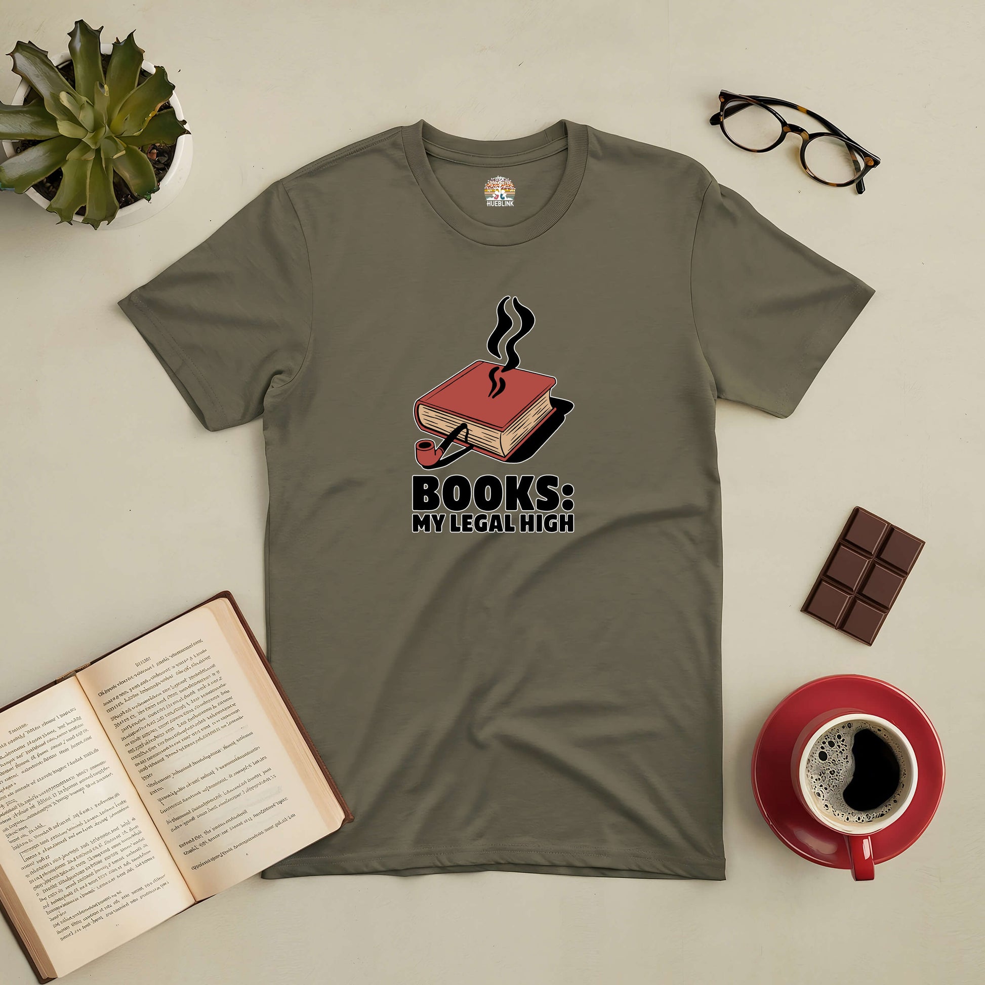 Olive green "Books: My Legal High" tee with book graphic, surrounded by an open book, glasses, coffee, and a plant.