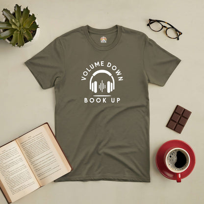 "Volume Down Book Up Tee with headphone graphic, surrounded by coffee, chocolate, glasses, and an open book"