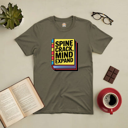 Olive green tee with "Spine Crack, Mind Expand" graphic, styled with an open book, glasses, chocolate, coffee, and plant.