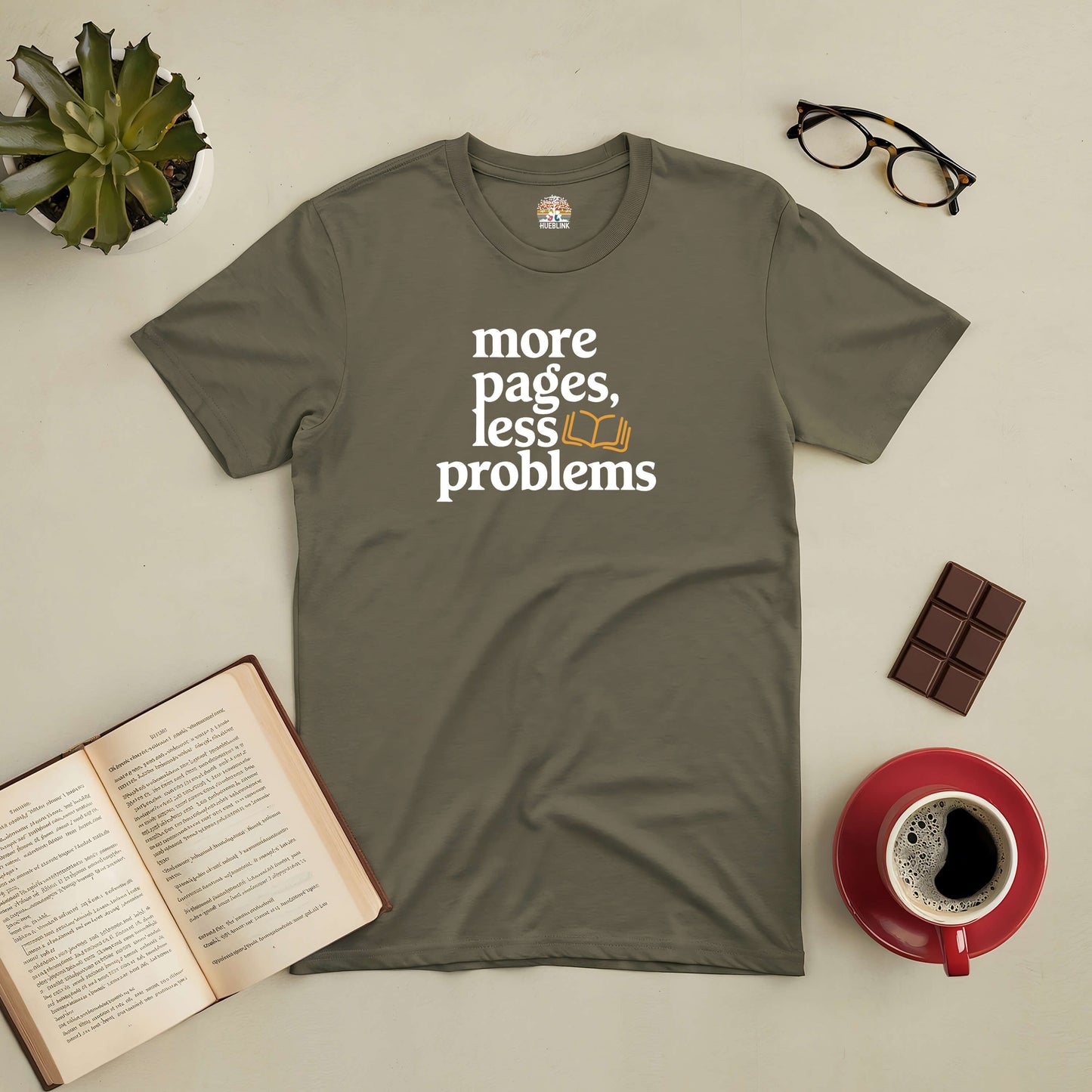 Olive green tee with "More Pages, Less Problems" text, ideal for book lovers. Styled with coffee, glasses, and an open book.