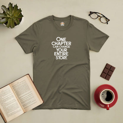 Olive green tee with "One Chapter Can Change Your Entire Story" text, alongside a book, coffee, glasses, and chocolate.