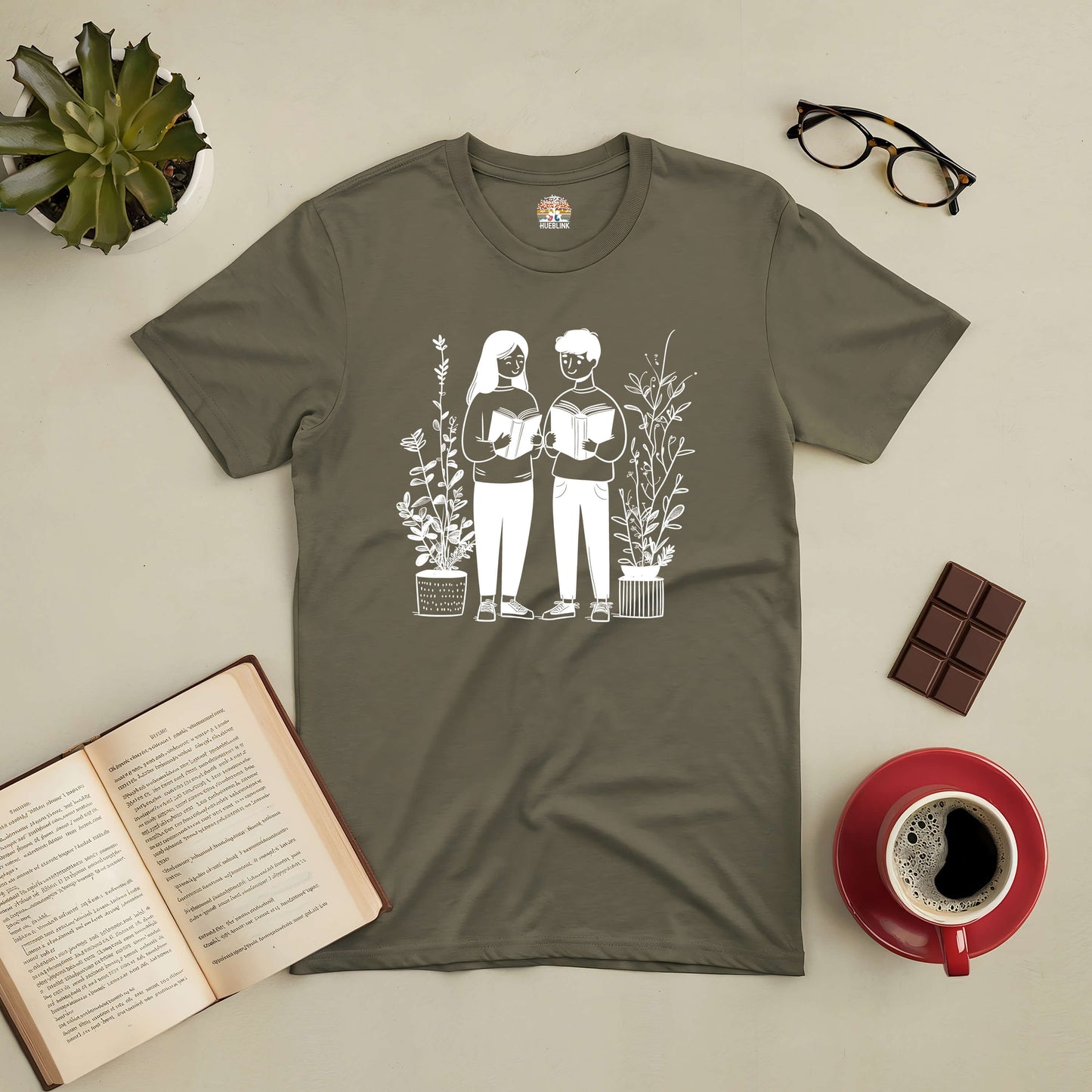 Bookish Buddies Tee with illustration of two friends reading, surrounded by books, coffee, and plants. Perfect for book lovers.