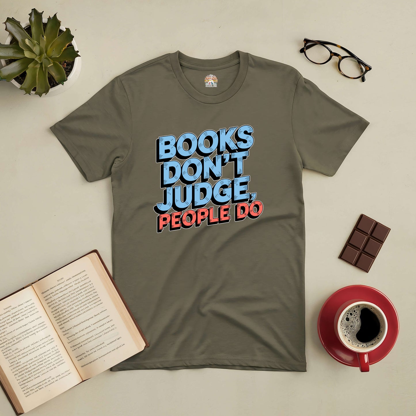 Olive green tee with text "Books Don't Judge, People Do" surrounded by an open book, chocolate, glasses, and coffee cup. Perfect for book lovers.