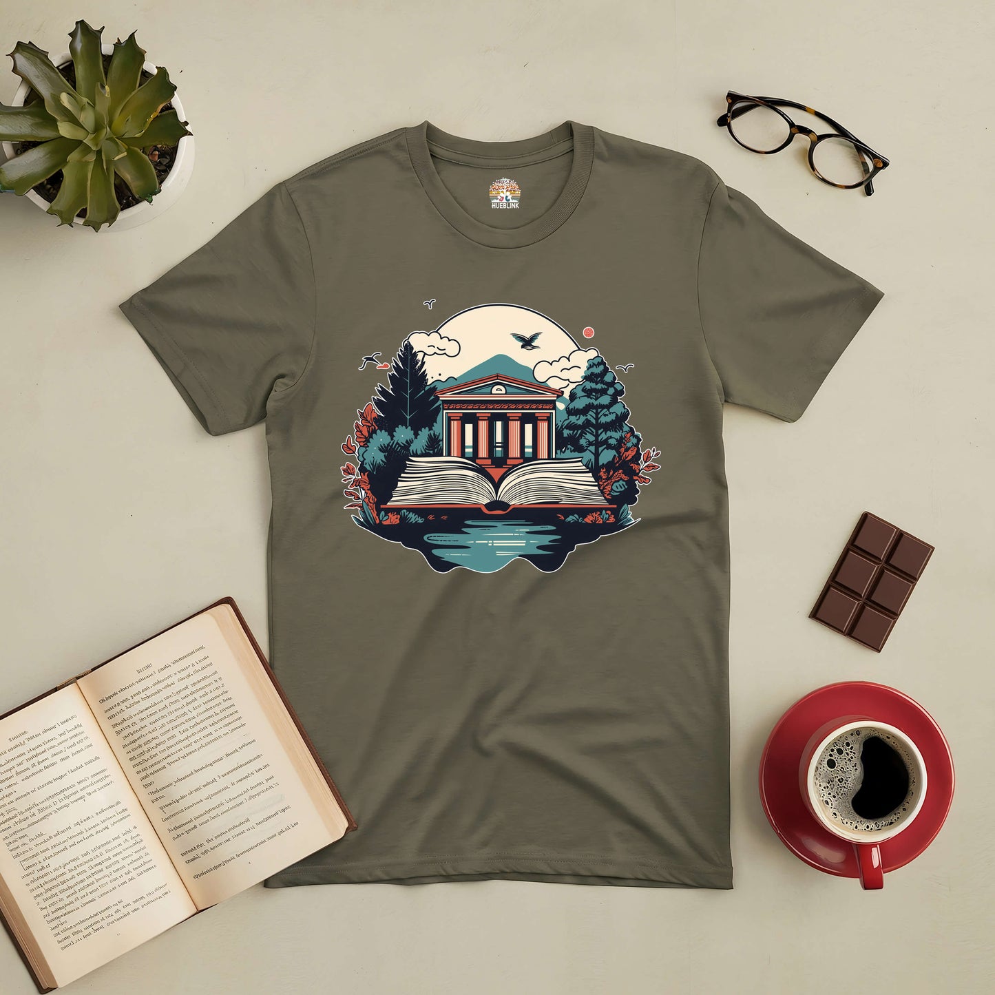 Gateway to Knowledge Tee showcasing a nature-inspired library design, surrounded by an open book, succulent, and coffee setup.