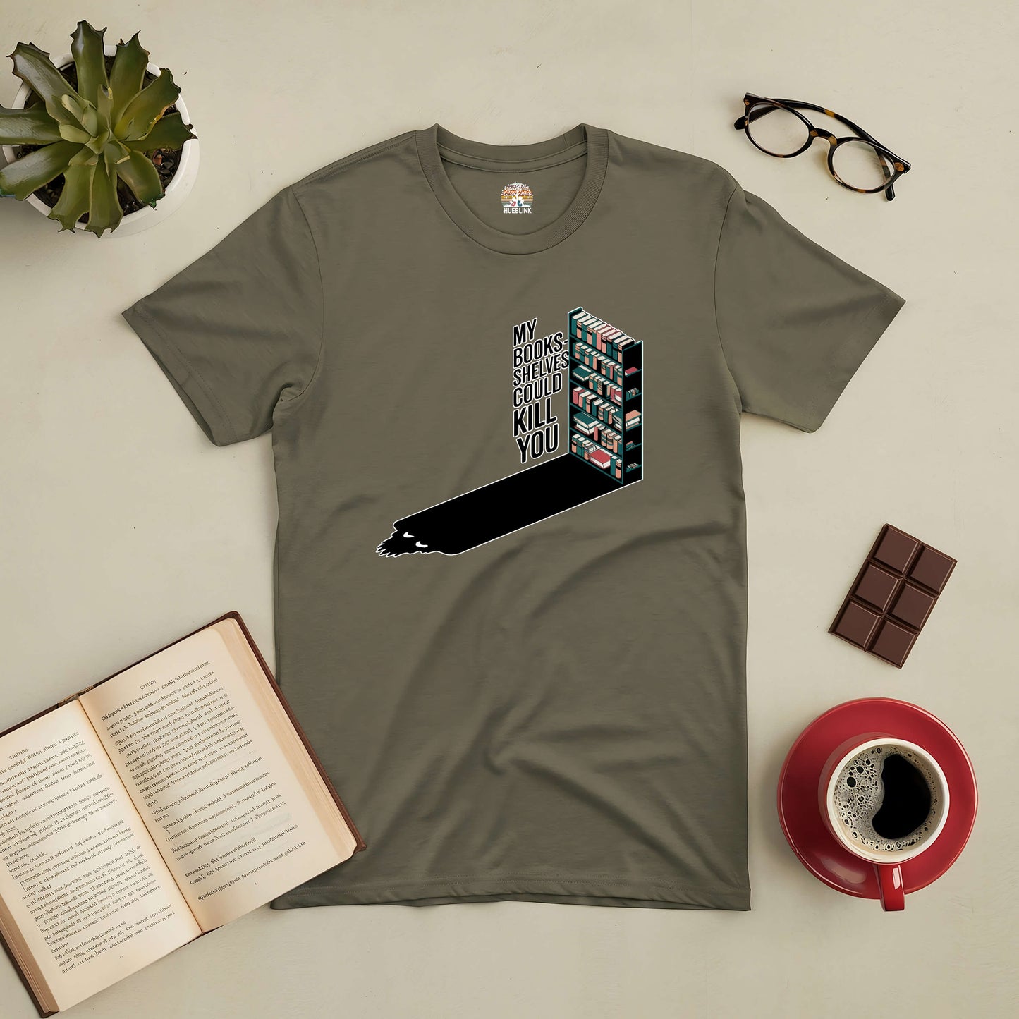 "My Bookshelves Could Kill You tee with bookshelf graphic, surrounded by book, coffee, and glasses on a table"