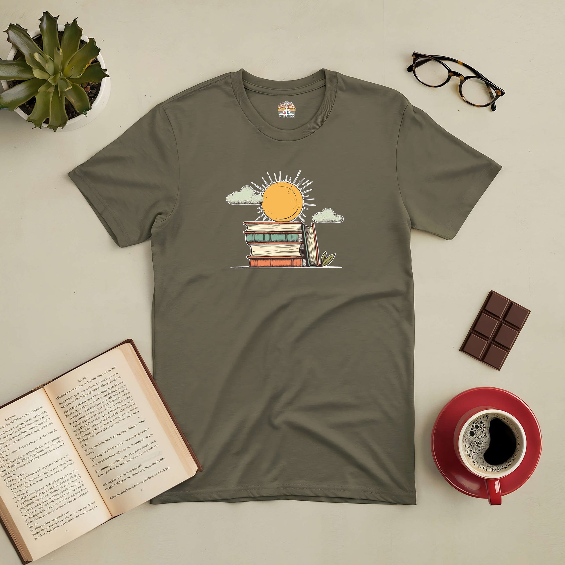 Olive "Literary Sunshine" tee featuring a sun over books, surrounded by coffee, chocolate, glasses, and an open book.