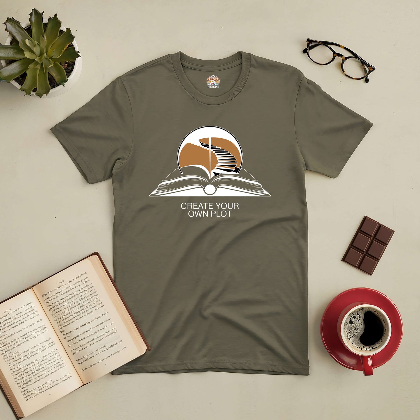 Olive green tee with "Create Your Own Plot" text, featuring an open book with a staircase, ideal for writers and dreamers.