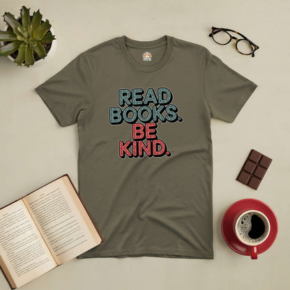 Green "Read Books. Be Kind." tee shirt on a table with book, glasses, chocolate, coffee, and plant. Perfect for book lovers.