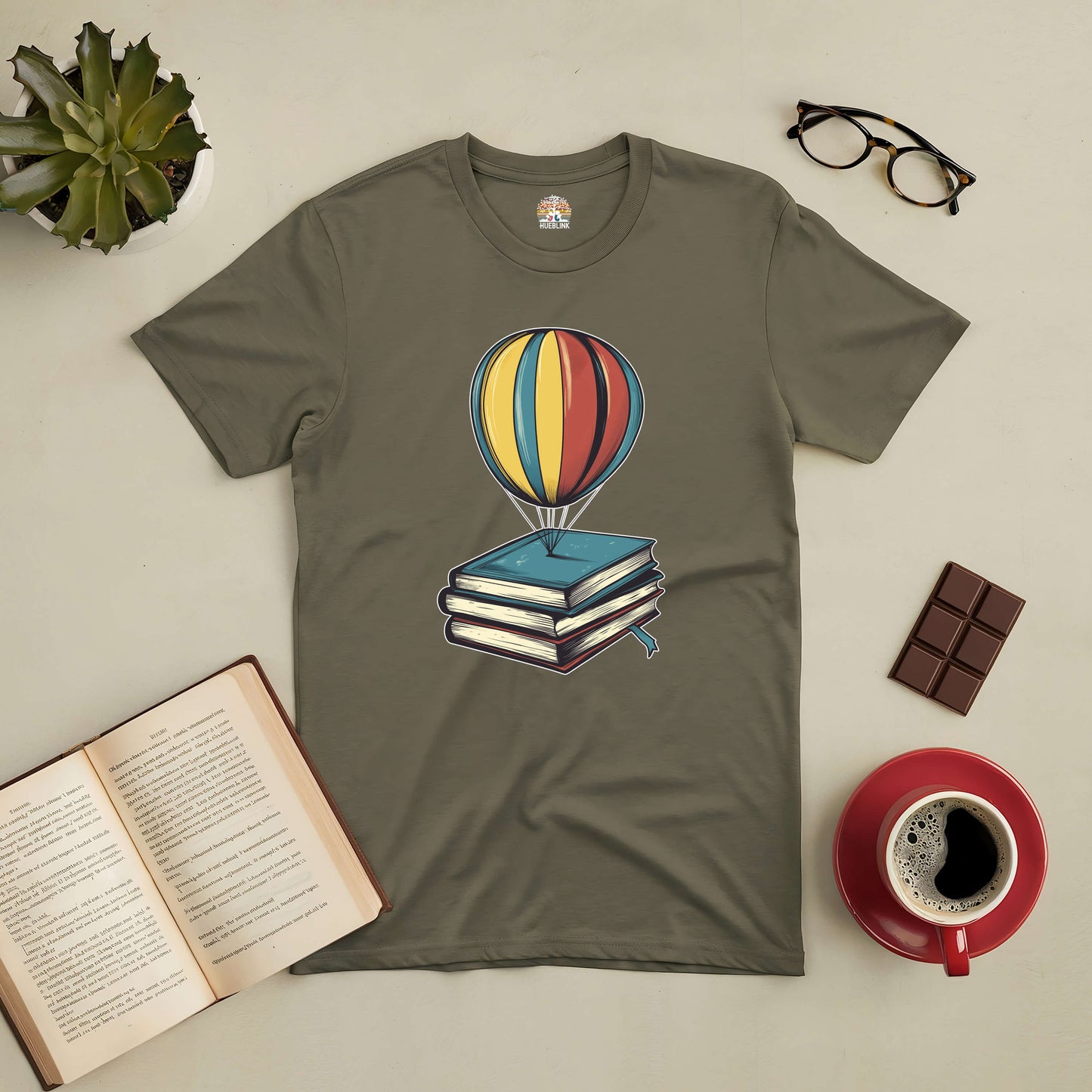 Olive green tee with a whimsical hot air balloon rising from a stack of books, symbolizing reading adventures.