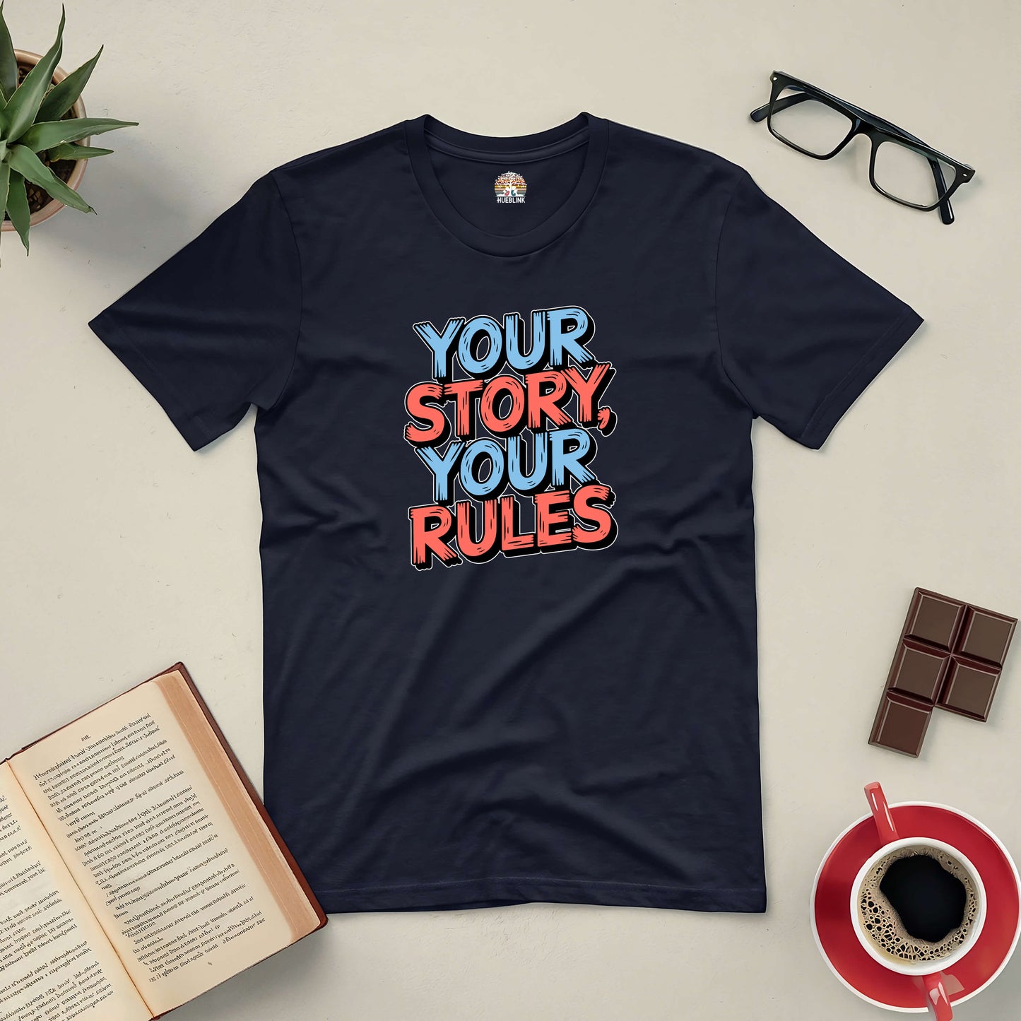 Black tee with "Your Story, Your Rules" text, surrounded by a book, glasses, and coffee, celebrating individuality.