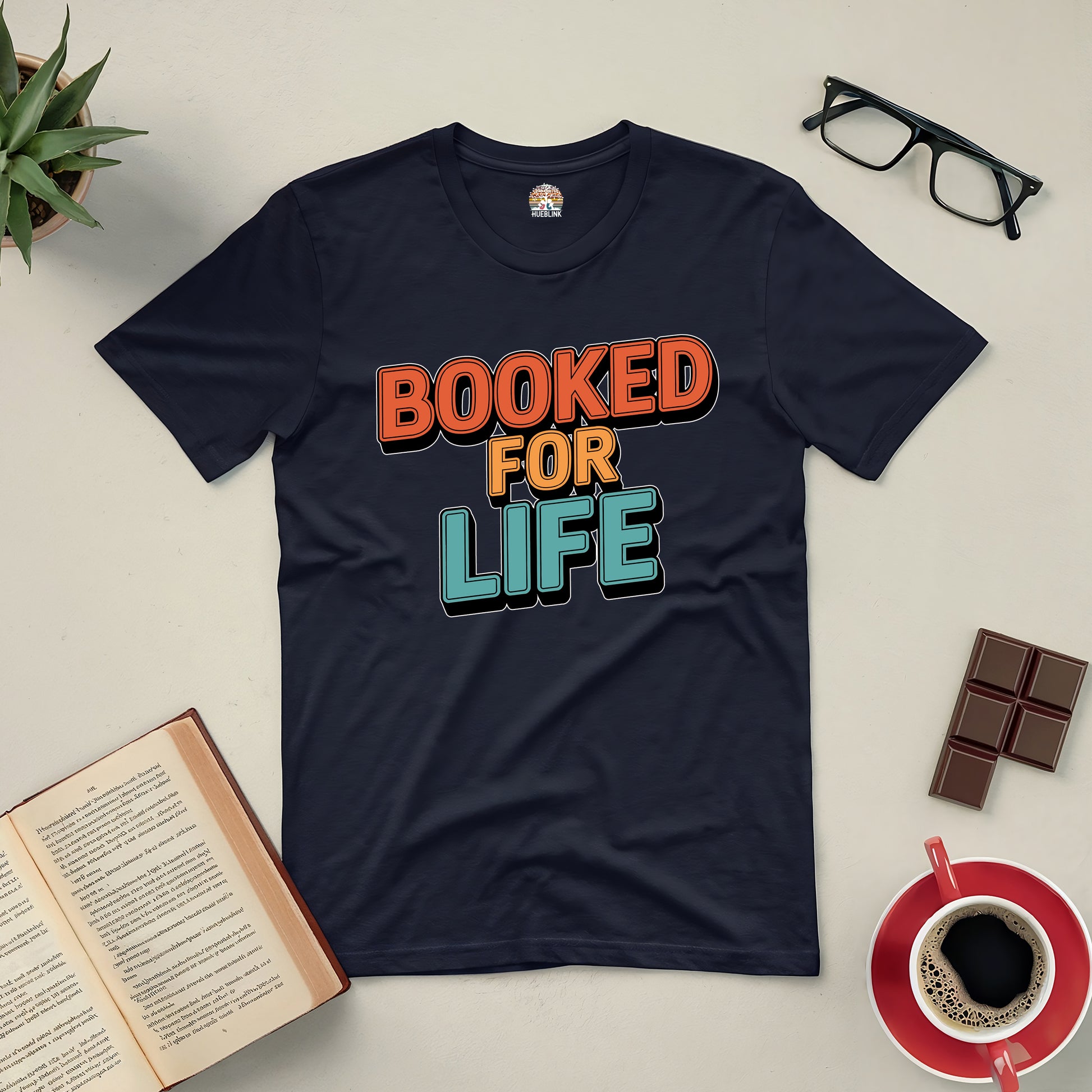 "Booked for Life tee for avid readers, featuring a bold design, surrounded by a book, glasses, chocolate, and coffee."