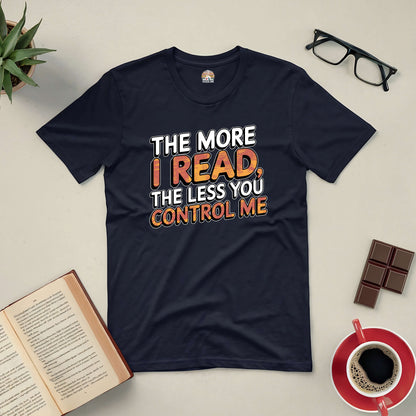 Black tee with "The More I Read, The Less You Control Me" text, surrounded by book, coffee, and glasses on a desk.