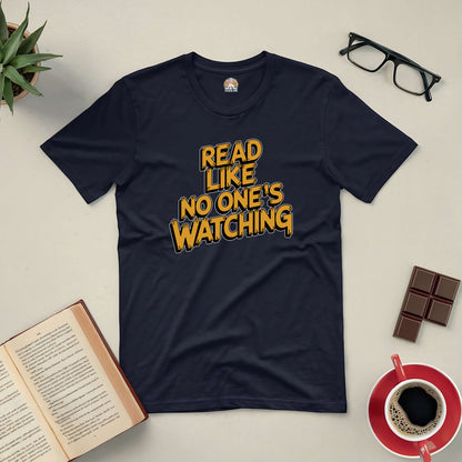 Black "Read Like No One's Watching" tee surrounded by glasses, book, coffee, and chocolate on a light surface.