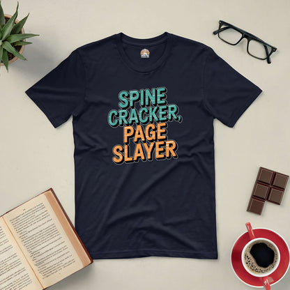 Black tee with "Spine Cracker, Page Slayer" text, surrounded by book, glasses, chocolate, plant, and coffee on table.