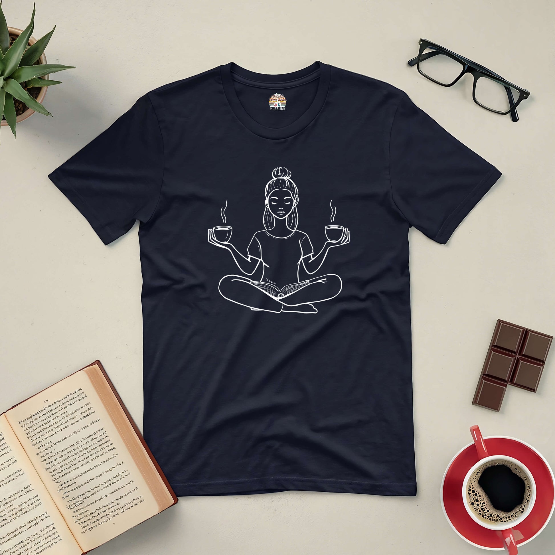 Perfectly Balanced Tee with meditative design, surrounded by a book, eyeglasses, coffee, and chocolate, symbolizing harmony and relaxation.