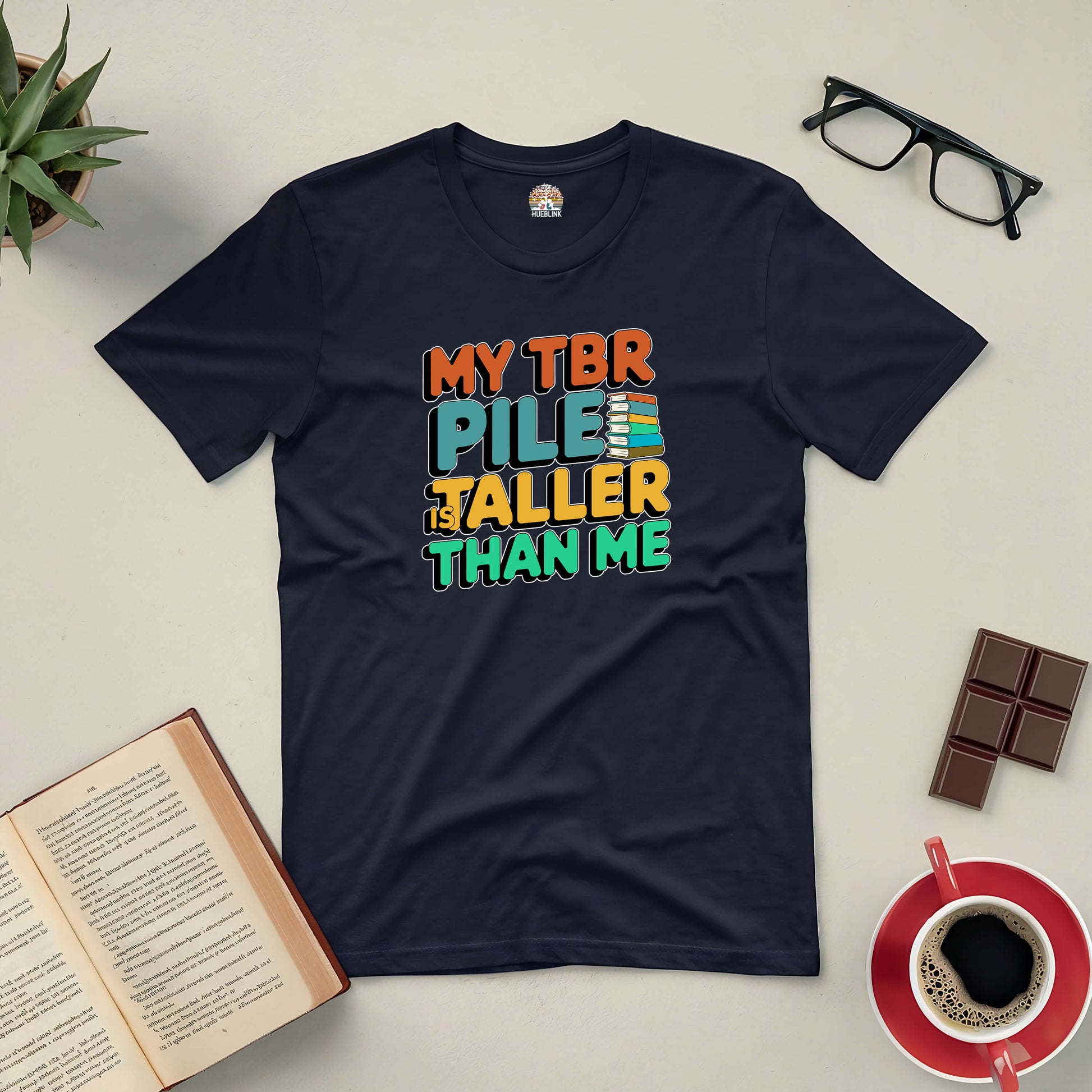 "My TBR Pile is Taller Than Me tee, perfect for book lovers with endless reading lists, surrounded by glasses, coffee, and an open book."