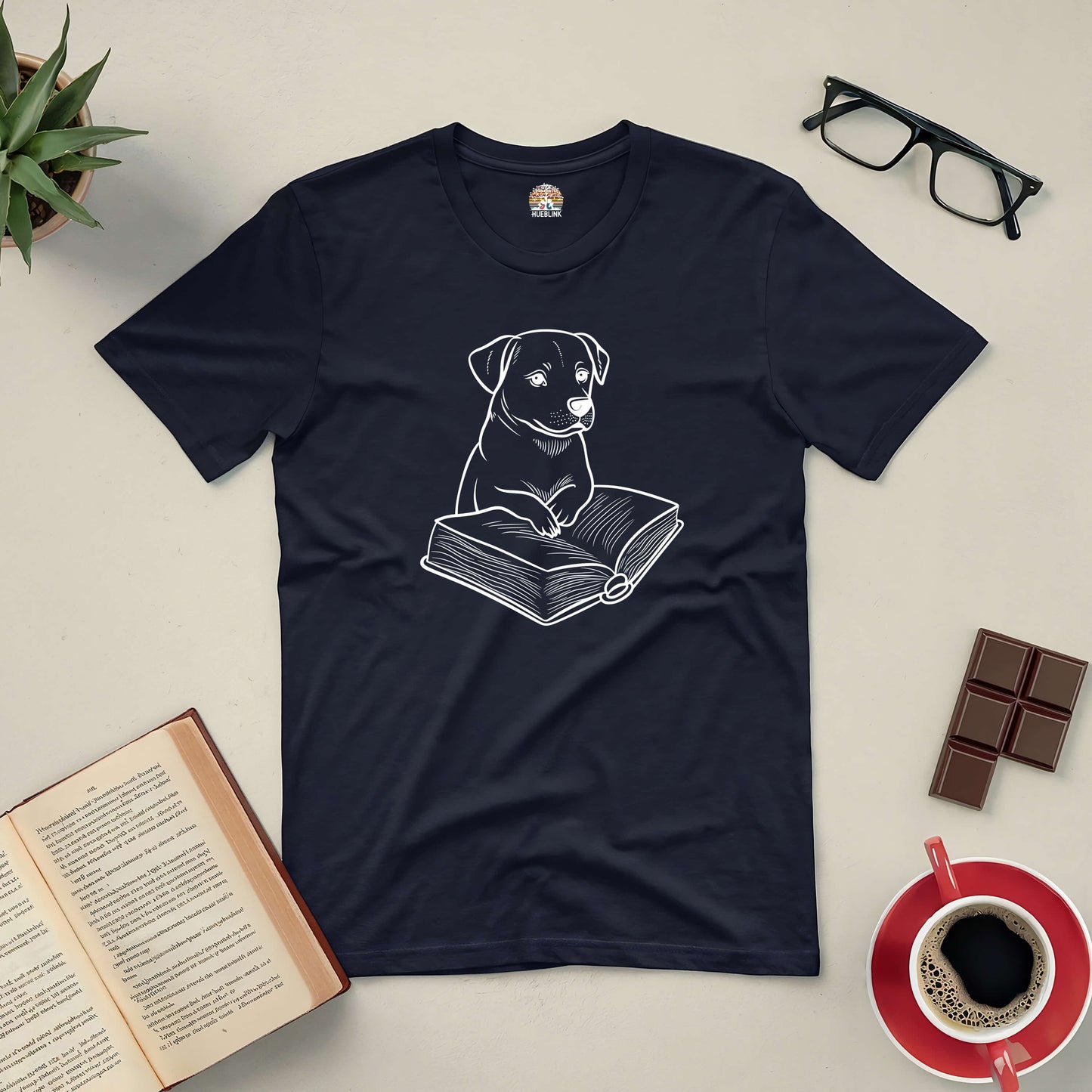 Black tee with a cute dog reading a book design, surrounded by glasses, coffee, chocolate, and an open book.