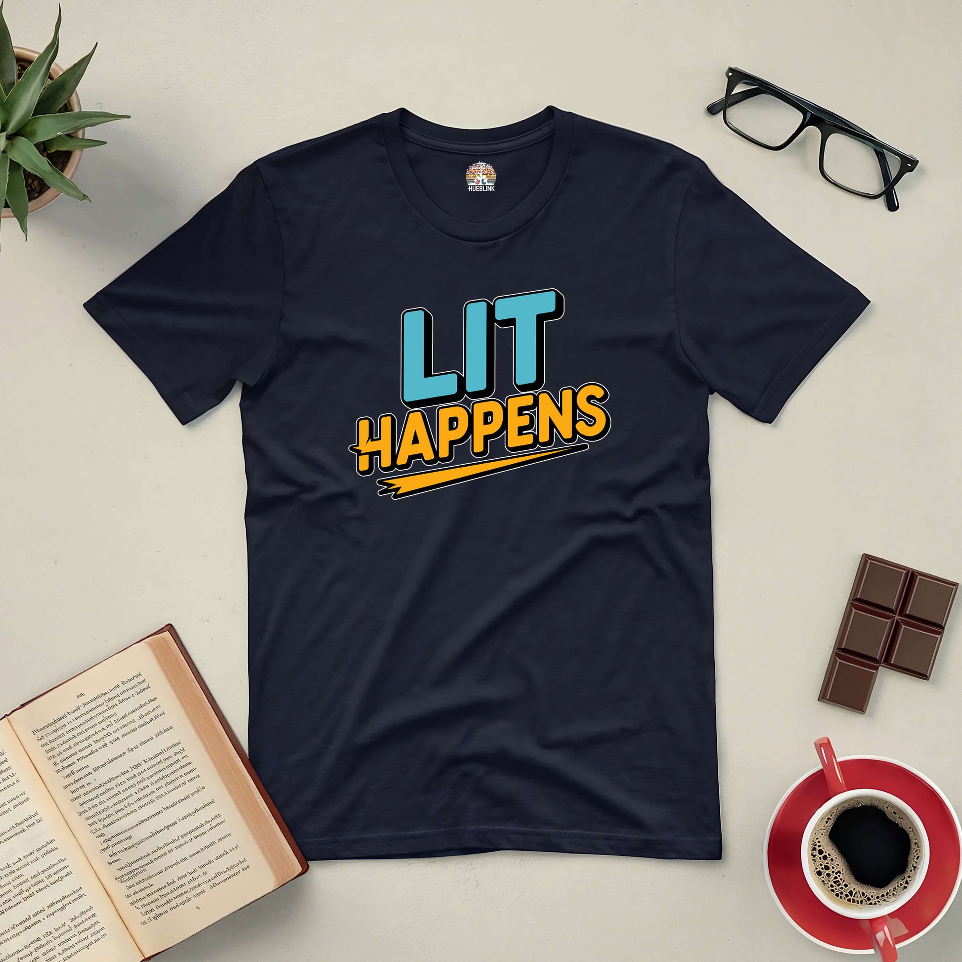 "Lit Happens Tee for book lovers with open book, glasses, coffee, and chocolate on a table"