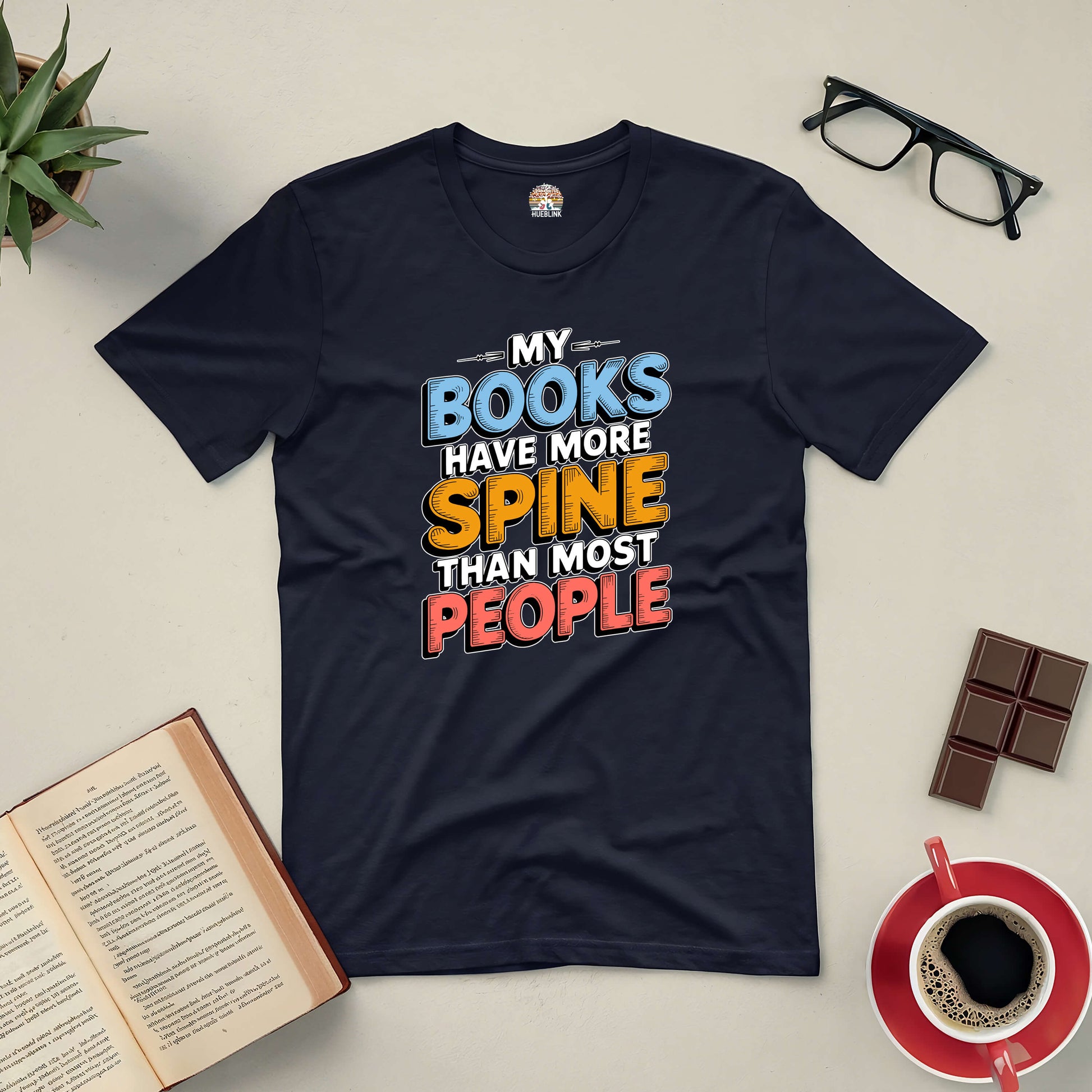 Black t-shirt with "My Books Have More Spine Than Most People" text, surrounded by open book, glasses, chocolate, and coffee.