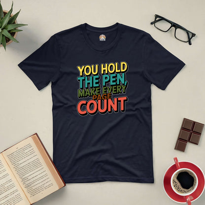 "You Hold the Pen, Make Every Page Count" tee on table with coffee, book, and glasses. Perfect for living with purpose.