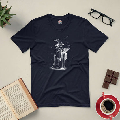 The Wizard's Grimoire Tee with mystical wizard design, displayed with book, glasses, and coffee setup. Perfect for fantasy lovers.