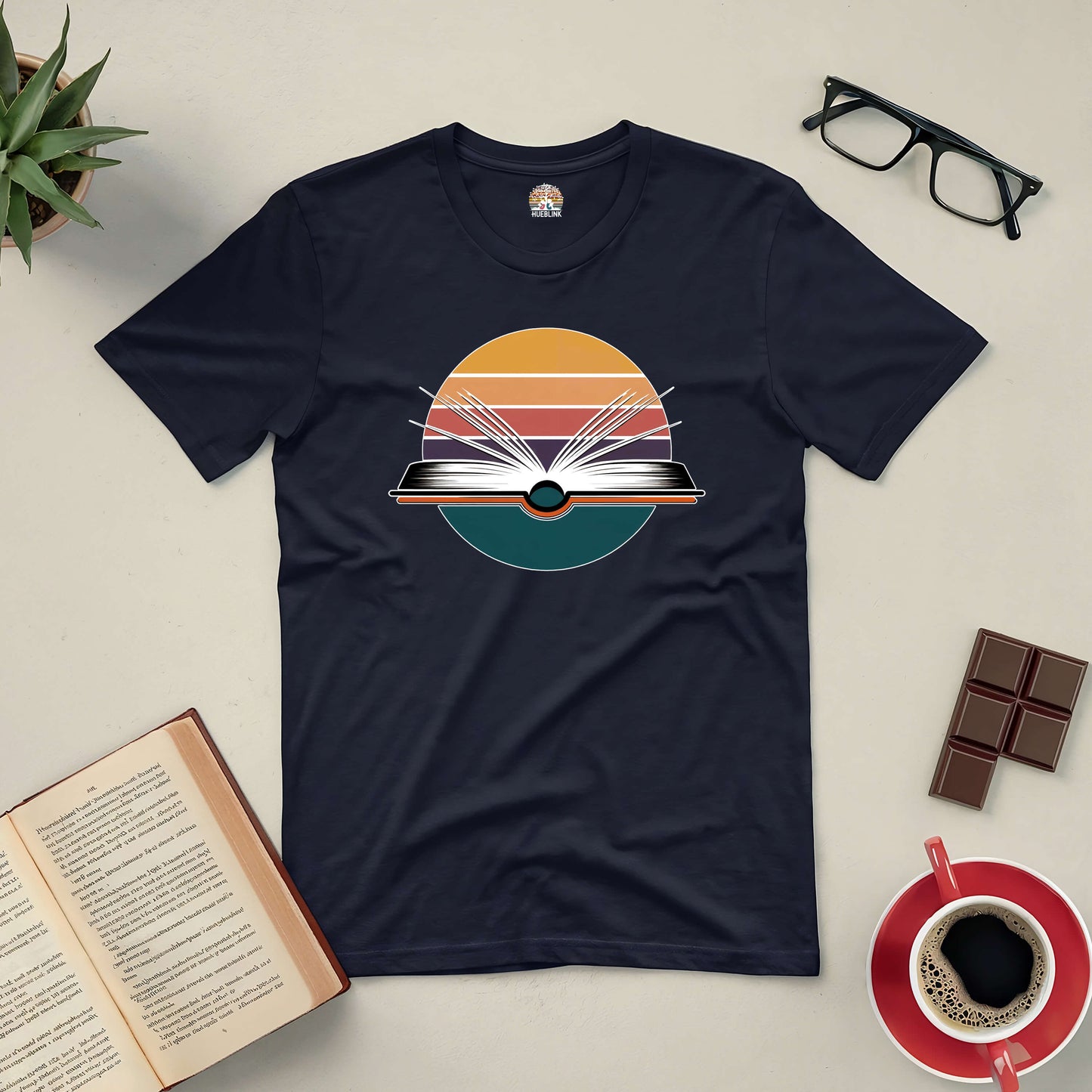 "Gateway to New Horizons Tee featuring open book graphic, surrounded by accessories like glasses, coffee, and chocolate."