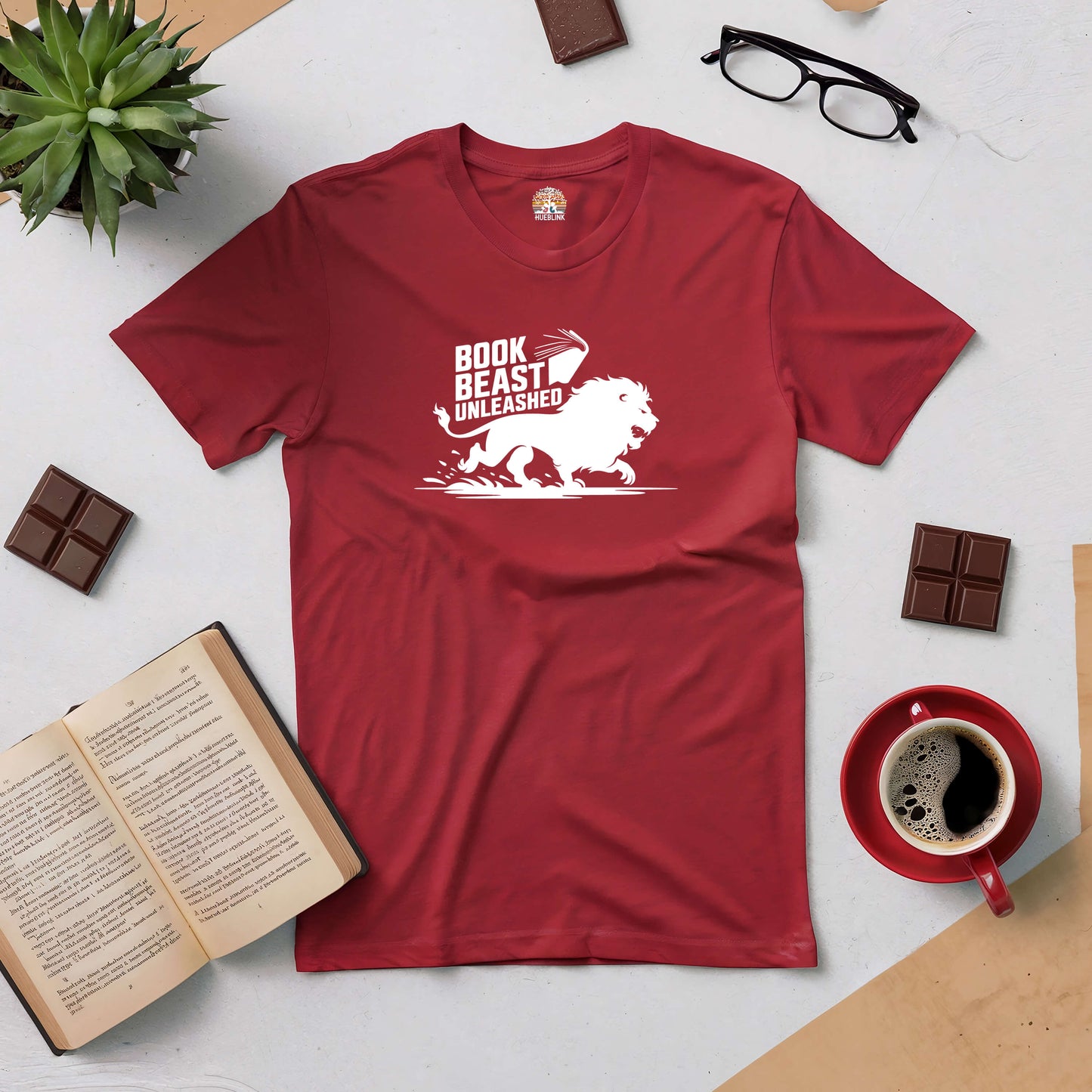 Book Beast Unleashed Tee with lion graphic, surrounded by coffee, glasses, and an open book, ideal for passionate readers.