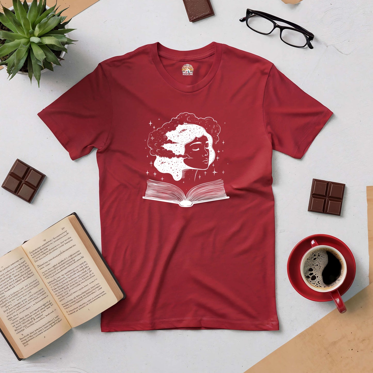 Red Universal Consciousness Tee with ethereal design featuring a cosmic face above an open book, surrounded by coffee and chocolates.